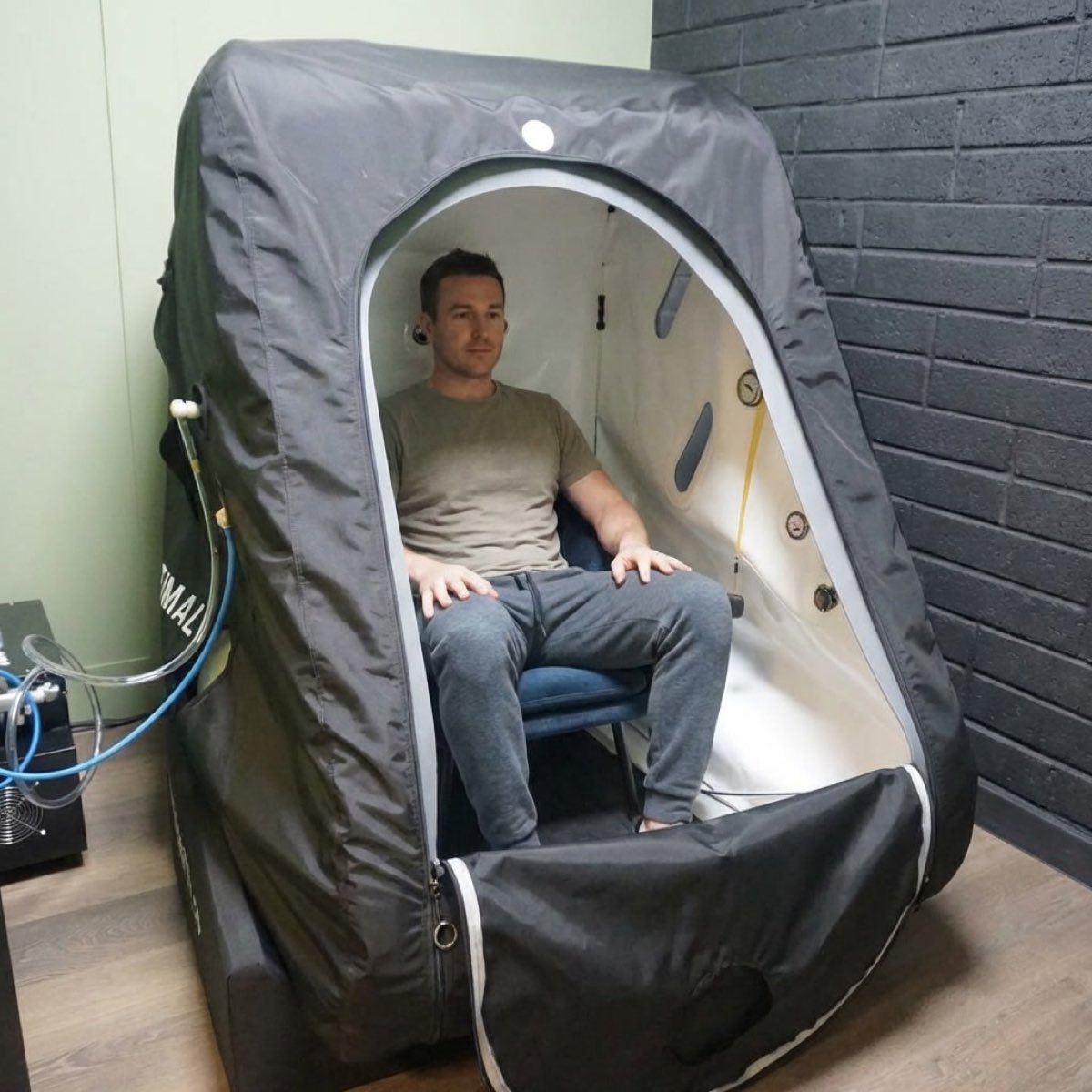A client seated in the open hyperbaric chamber, hands on his knees