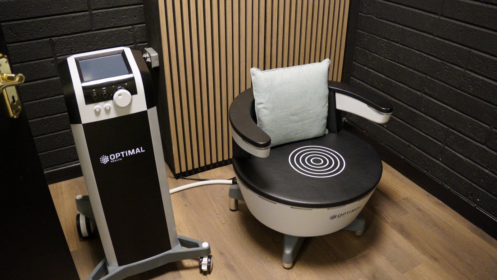 The HIFEM chair and its console, empty, against wood slats and black brick