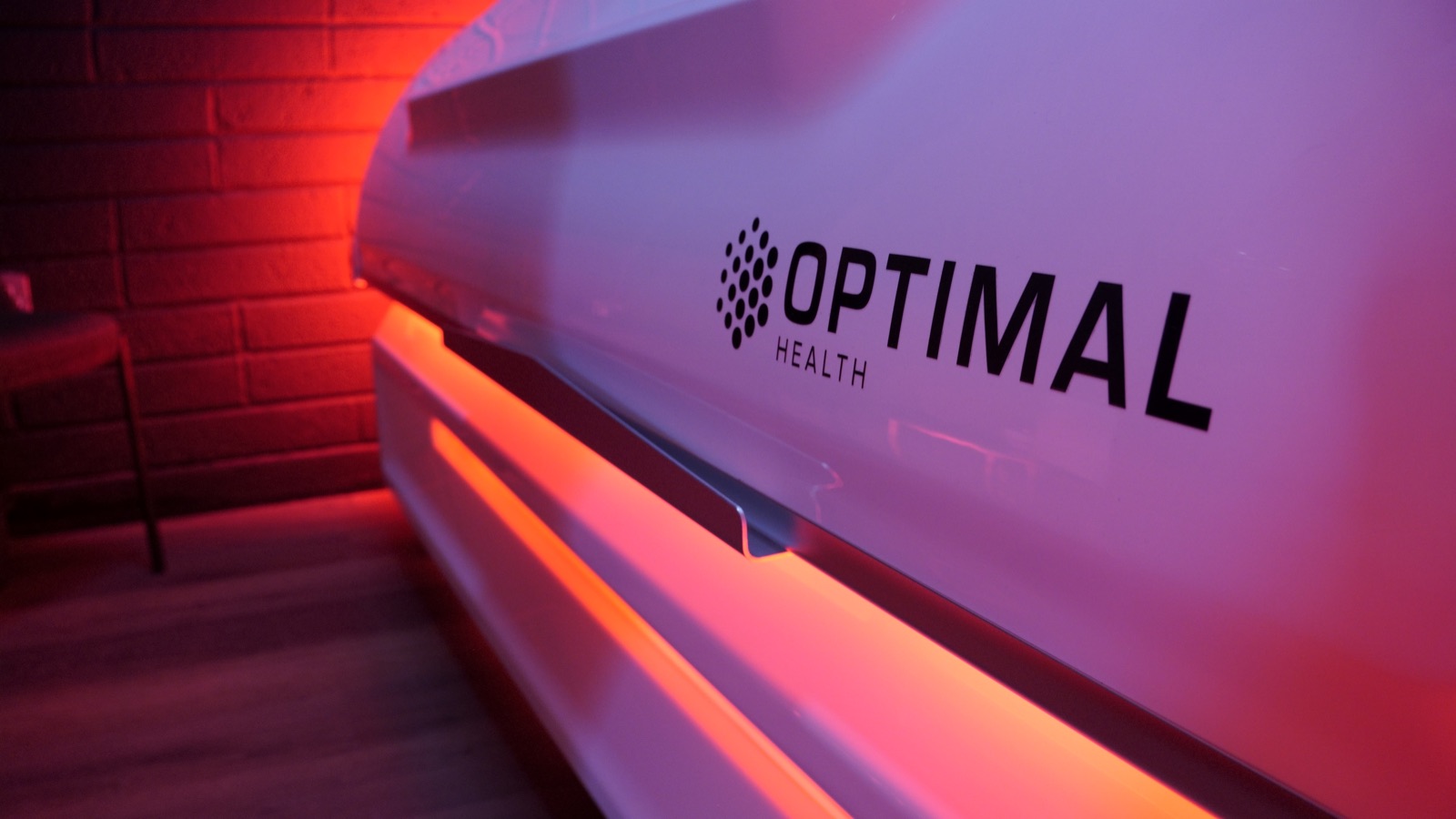 The Optimal Health name on the shell of the infrared bed, under a red wash